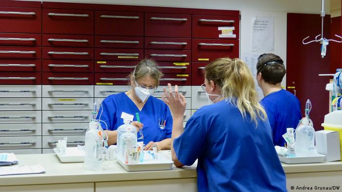 Андреа Крауткремер е медицинска сестра в интензивно отделение в Кобленц От началото на пандемията натоварването там е изключително тежко. Болните страдат далеч не само от Ковид-19. Дойче Веле прекара един ден с нея в болницата. В 4:00 будилникът на Андреа Крауткремер звъни. В 5:45 вече е на работното си място. 54-годишната германка работи като медицинска сестра в едно от интензивните отделения на болницата "Мариенхоф" в Кобленц от над три десетилетия. Междувременно само на половин работен ден. На фона на голямото физическо и психическо натоварване от началото на пандемията тя не иска да работи на пълно работно време. Но не спира да подчертава колко много обича професията си. Огромно физическо и психическо натоварване От коридора се виждат пациентите, разделени един от друг с високи стъклени прегради. В момента 11 от 12-те легла за изключително тежки случаи са заети. Три от тях - от пациенти с Ковид-19. "Около Коледа натоварването беше несравнимо", спомня си Андреа Крауткремер и добавя, че тя и колегите ѝ са били в състояние да извършват единствено основното медицинско обслужване. "Ако винаги трябваше да се работи така, днес вече нямаше да съм тук", казва Андреа Крауткремер. "През март 2021 година болните от Ковид-19 са по-малко. Леглата се пълнят с пациенти с инфаркти и инсулти, както и с хора за планови операции, които болница "Мариенхоф" отново изпълнява", обяснява Курт Зимон, който завежда две интензивни отделения. Той е доволен, че за момента има кой да изпълнява смените въпреки дефицита на кадри. Работата на медицинските сестри и болногледачите сякаш не е ценена достатъчно от обществото, казва Зимон и подчертава: "Добрата грижа струва пари". Нужно е много повече признание за тези кадри, смята той. В началото на работния ден Андреа Крауткремер е на съвещание с колегите си. На него медицинските сестри и болногледачите от застъпващата смяна получават информация за пациентите, обсъждат състоянието им и решават кой какви задачи да получи. На този ден на легло номер 1 и 2 има пациенти с Ковид-19, които са на обдишване. Пациентът от легло номер 4 е в "максимално тежко състояние". А пациентът от легло номер 8 в състояние на делириум е откъснал системата от ръката си и е захапал една от тръбите. Освен това линейката е довела мъж, за когото се подозира, че е болен от коронавирус. Той е настанен в една от изолационните стаи. След съвещанието става ясно: днес Андреа поема ръководството на смяната, двама от пациентите, както и придружаването на нова практикантка. "Хубаво дишайте през носа" Преди да се срещне с първия пациент за деня, Андреа Крауткремер си прави бърз тест за коронавирус. Тя се тества веднъж седмично. Повечето от колегите ѝ са ваксинирани, но по време на имунизациите тя е била под карантина. Към 7:30 часа, преди да влезе в стаята на Мартин Фабер (името е променено), Андреа слага защитно облекло, два чифта ръкавици и шлем над маската FFP2. Днес тя ще го посети четири пъти, всеки път ще облече защитно облекло, ще го свали отново много внимателно и ще го изхвърли. Господин Фабер е на малко над 50 години, болен е от левкемия и е настанен в отделението от три дни. Майка му е починала от Ковид-19 през януари, на едно легло разстояние от неговото. Когато вратата на стаята се затвори, се чува звукът на машината за обдишване. "Добро утро, господин Фабер, как мина нощта?", поздравява Андреа с усмивка. "Добре", отговаря той под маската. "Хубаво е, че издържахте толкова дълго по корем." Пациентът лежи по корем от предния ден за постигане на по-добро обдишване на белите дробове. Апаратът, към който е включен, се казва "Елиза". Той наблюдава сърдечната честота, кръвното налягане и насищането с кислород. Това е една от многото машини, с които боравят медицинските сестри в "Мариенхоф". В случай на бъбречна недостатъчност се използва и апарат за диализа. А в краен случай и ECMO, при който кръвта се обогатява с кислород извън тялото. Андреа проверява мониторите, почиства тялото на господин Фабер внимателно с предварително затоплени кърпи за еднократна употреба и оправя леглото му. След това контролира вливанията, дава лекарства, подрежда многото тръбички. Обсъждат как той иска най-накрая да се ожени за партньорката си, за предпочитане веднага, говорят и за неговите котки, които у дома много обичат да лежат на корема му. За да може да закуси, Андреа Крауткремер вдига вентилационната маска от лицето на Мартин Фабер. Той въздъхва с облекчение: "О, това е приятно!". Сестрата веднага поставя тънката тръбичка, с която друга машина вкарва кислород в носа му: "Хубаво дишайте през носа". Пациентът закусва и говори по телефона, медицинската сестра подрежда стаята. Тук разпределят лекарствата Тук разпределят лекарствата Малко след като Андреа му е поставила отново маската, звъни партньорката на пациента, за да научи какво е състоянието му. "Тя може да се обади по всяко време", обяснява Андреа и добавя: "Разговорите с близките са много важни". От болницата са закупили таблети, за да улеснят контакта по време на забраната за посещения, наложена заради пандемията. Персоналът в интензивните отделения трябва да документира всичко, което прави - заради сигурността на пациентите и плащанията на здравните каси. И всичко това на фона на постоянен шум, издаван от апаратите за наблюдение и от компютрите, на които се отчитат показателите на пациентите. Цяло чудо е как болногледачите успяват да не пропуснат някой важен сигнал. При всяка една аварийна индикация някой реагира веднага. "Тук е много стресиращо", казва Андреа Крауткермер, "но благодарение на страхотния екип се издържа". Работата на медицинските сестри далеч не е свързана само с обслужването на настанените пациенти. Телефонът често звъни, линейки карат нови болни, пристигат и големи кутии с лекарства, които трябва да бъдат сортирани. Освен това в случай че някое устройство се развали, сестрите и болногледачите веднага трябва да уведомят техниците. Ежедневно се водят и разговори с кухнята - оттам питат каква храна могат да приемат пациентите. А и планът на леглата постоянно трябва да се актуализира. "Смъртта е част от живота" В 9:20 Андреа Крауткремер включва траурната лампа на регистратурата. "За съжаление пациентът на легло 4 умира", казва тя. Лечението е преустановено, двама роднини са при него. Посещенията на роднини са позволени само при умиращите пациенти. Топлата светлина, която лампата излъчва, е сигнал "за малко повече тишина", обяснява началничката на смяната. "Не може да работиш в интензивно отделение, ако не приемаш, че смъртта е част от живота." Когато тази лампа свети, всеки тук знае: починал е пациент Когато тази лампа свети, всеки тук знае: починал е пациент Андреа обаче няма повече време да мисли за живота и смъртта. Съобщават ѝ, че пациентът на легло 1, който е болен от коронавирус, се влошава. През коремната стена трябва да бъде поставена стомашна сонда. Прави се и разрез на трахеята, тъй като пациентът трябва да получи трахеостомната канюла за вентилация. Въпреки всички усилия пациентът губи битката с вируса: два дни по-късно той умира. "Правиш всичко, което е по силите ти - но то не е достатъчно" - така Андреа коментира тази ситуация, в която е изпадала неведнъж. Няколко дни по-късно разговаряме с нея по телефона. Още един пациент е починал. Много от колегите ѝ вече са на ръба - преумората, тежко болните пациенти и страхът от заразяване си казват своето. "Да" и последно сбогом Андреа разказва и за Мартин Фабер. Лекарите го посъветвали да не чака дълго за сватбата. Свещеникът на болницата звъннал в службата по вписванията, откъдето изпратили служител. Свещеникът купил червени рози, медицинските сестри донесли пенливо вино. А Андреа украсила стаята на пациента със сърца и празнични панделки. Двамата младоженци се врекли във вечна вярност. По лицата на присъстващите се стичали сълзи. Андреа ни разказва, че през следващите дни състоянието на господин Фабер се подобрило, но малко след това показателите се влошили сериозно. Наложили се диализа и интубация. Седмица след сватбата Мартин Фабер издъхнал. Сега той ще бъде погребан заедно с майка си - нейното погребение било отложено до изписването му.